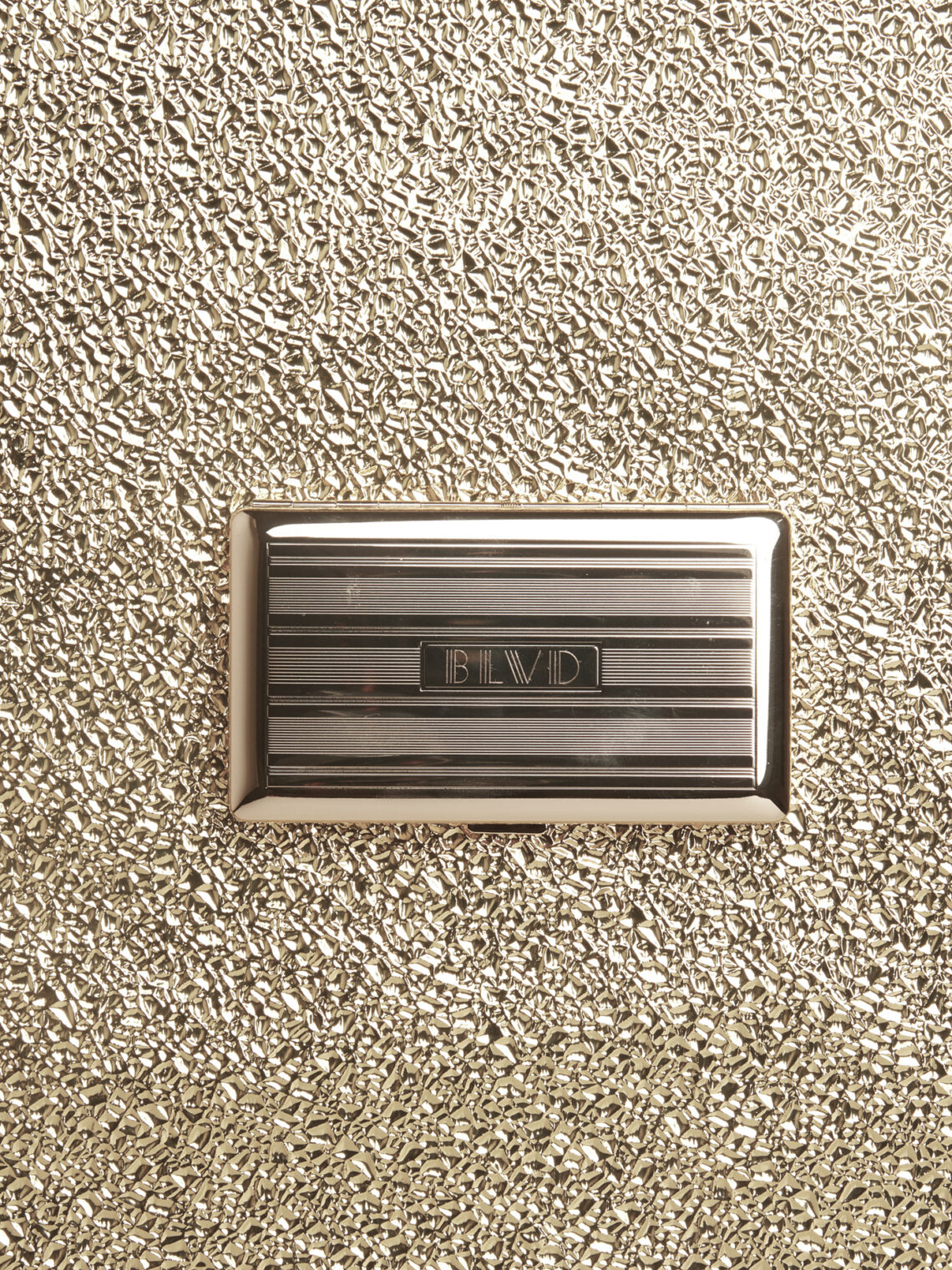 Polished gold metallic check presenter with BLVD branding resting on a textured gold surface.