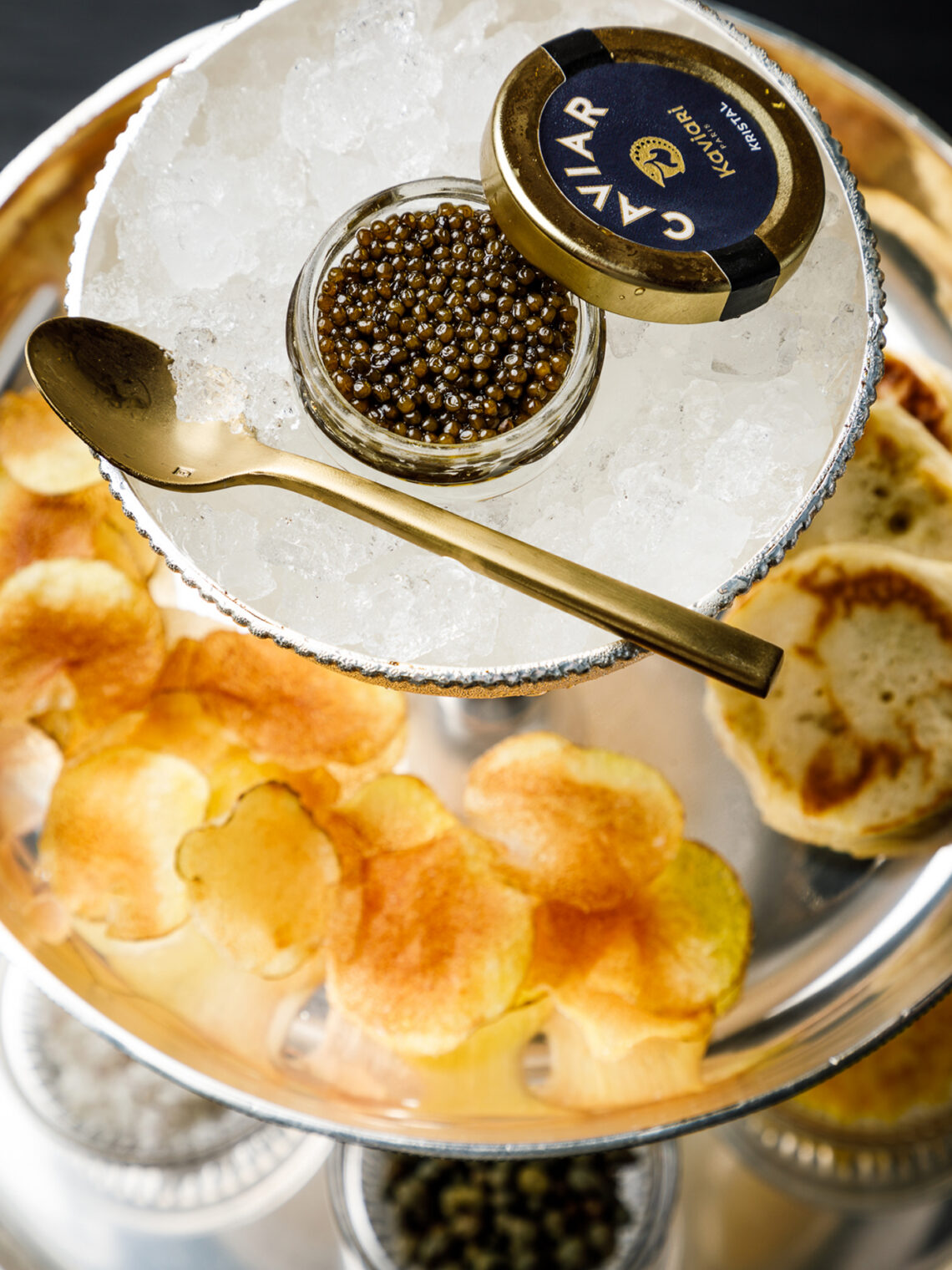High-angle view of caviar served over ice with blinis and potato chips.