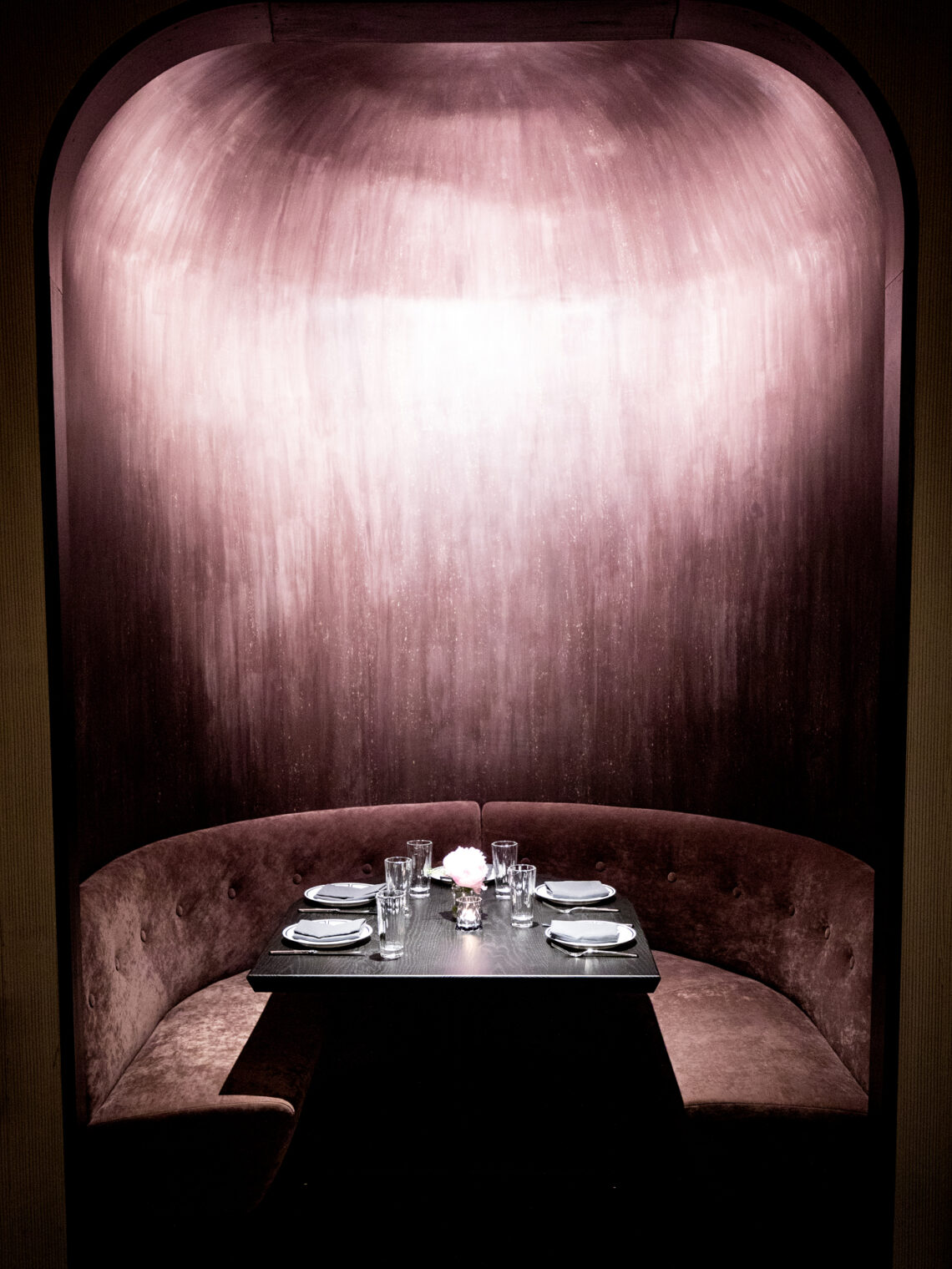 Luxurious, dimly lit circular velvet dining booth nestled inside a private arched alcove.