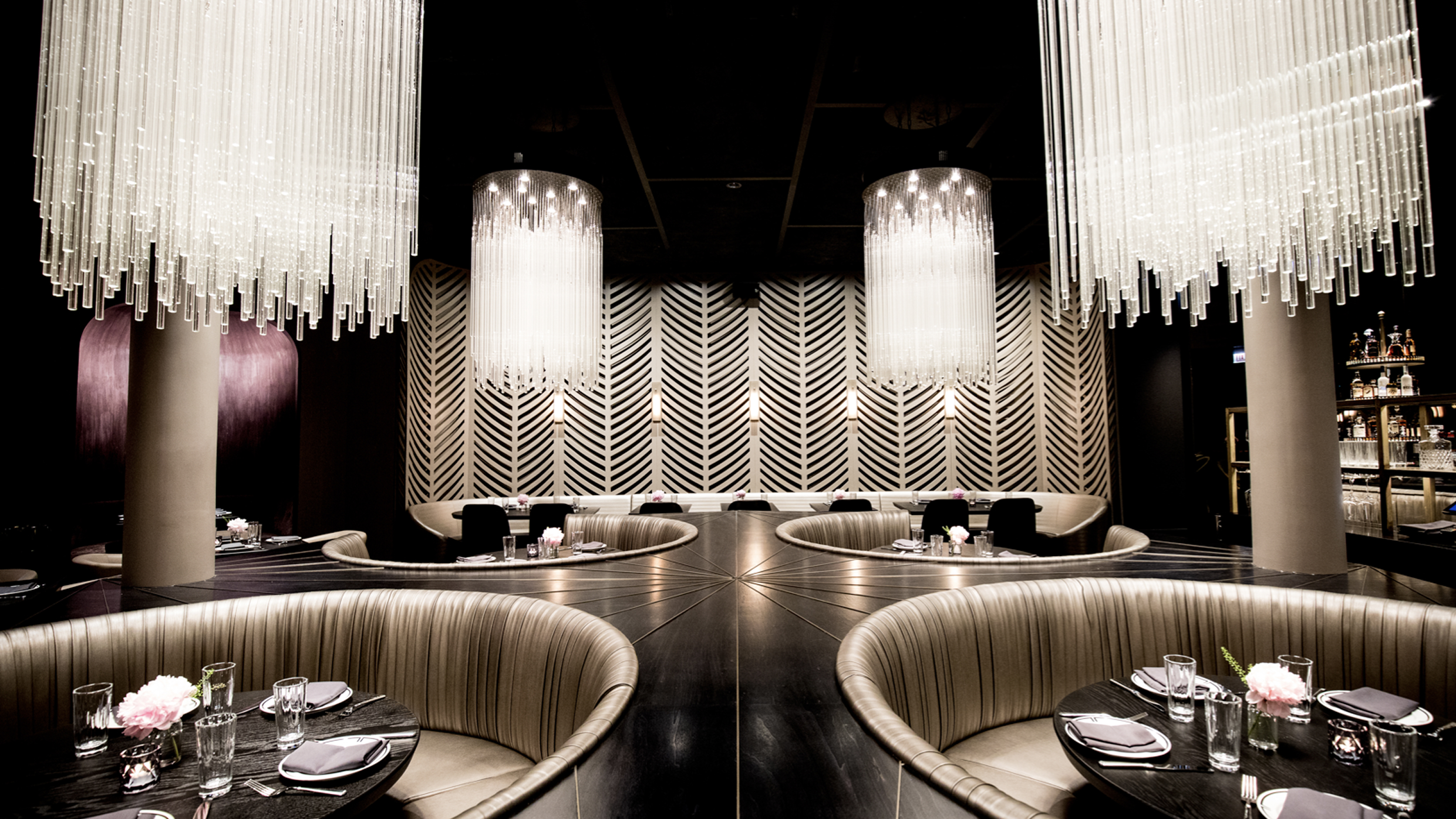 Upscale modern dining room with circular booths and striking overhead glass rod light fixtures.