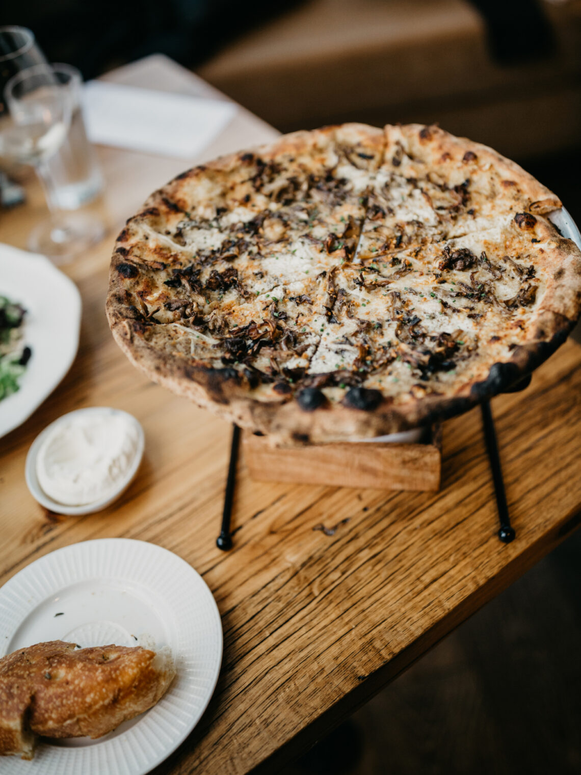 Whole mushroom and cheese pizza served on a metal stand over a wooden table.