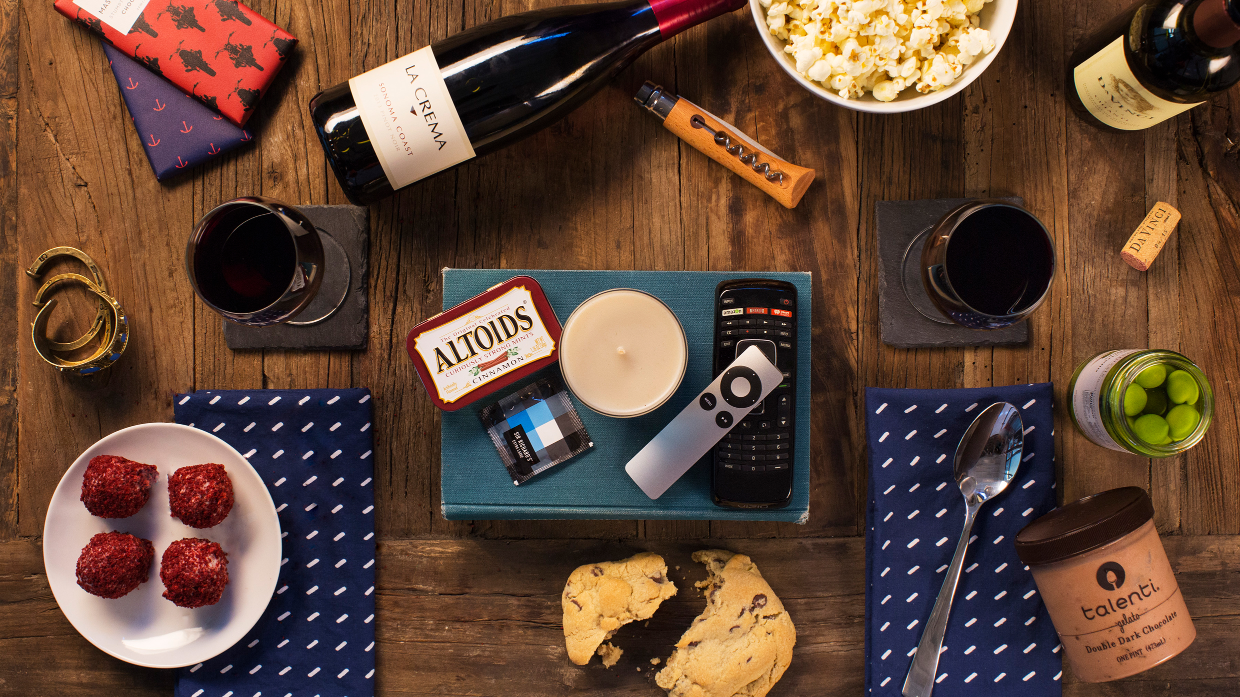 Overhead flat lay of snacks, wine, a candle, and a television remote.