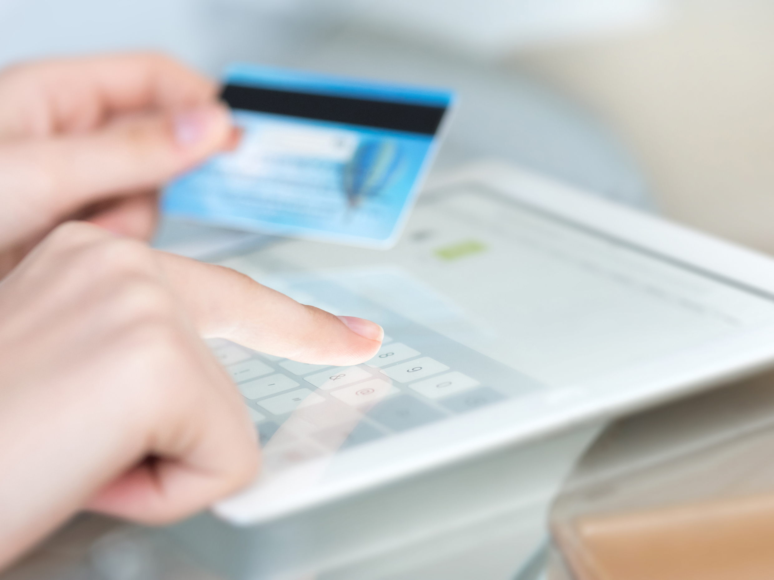 Close-up of hands typing on a tablet while holding a blue credit card.