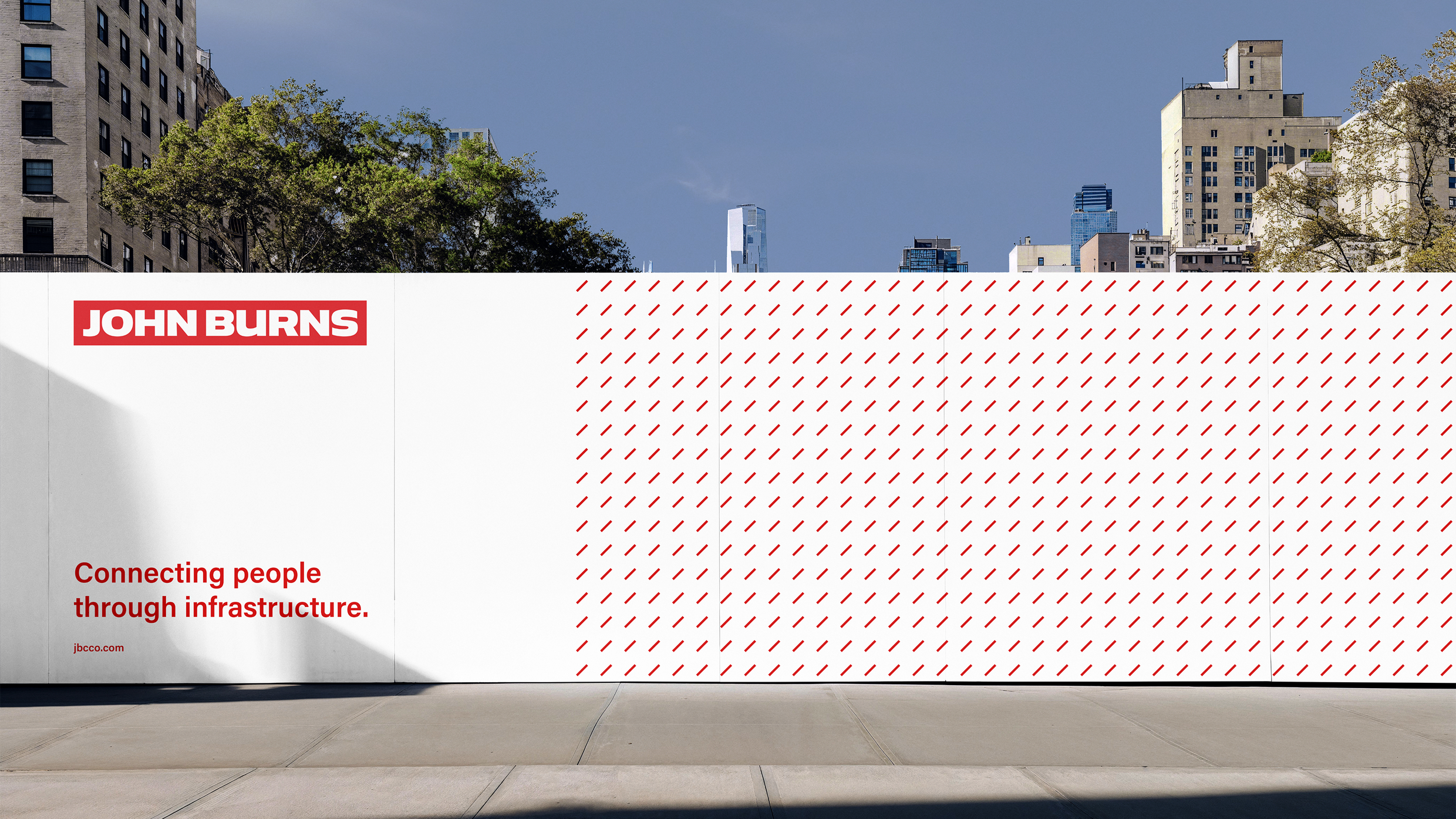 Construction site fence hoarding featuring John Burns branding and corporate infrastructure slogan.