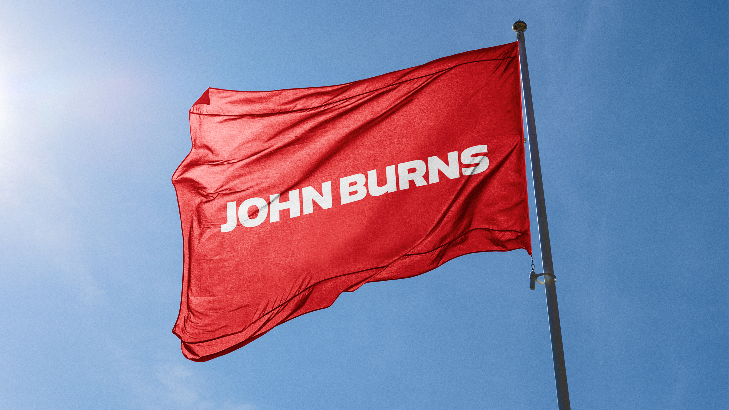 Red corporate flag with white John Burns logo waving against a clear blue sky.