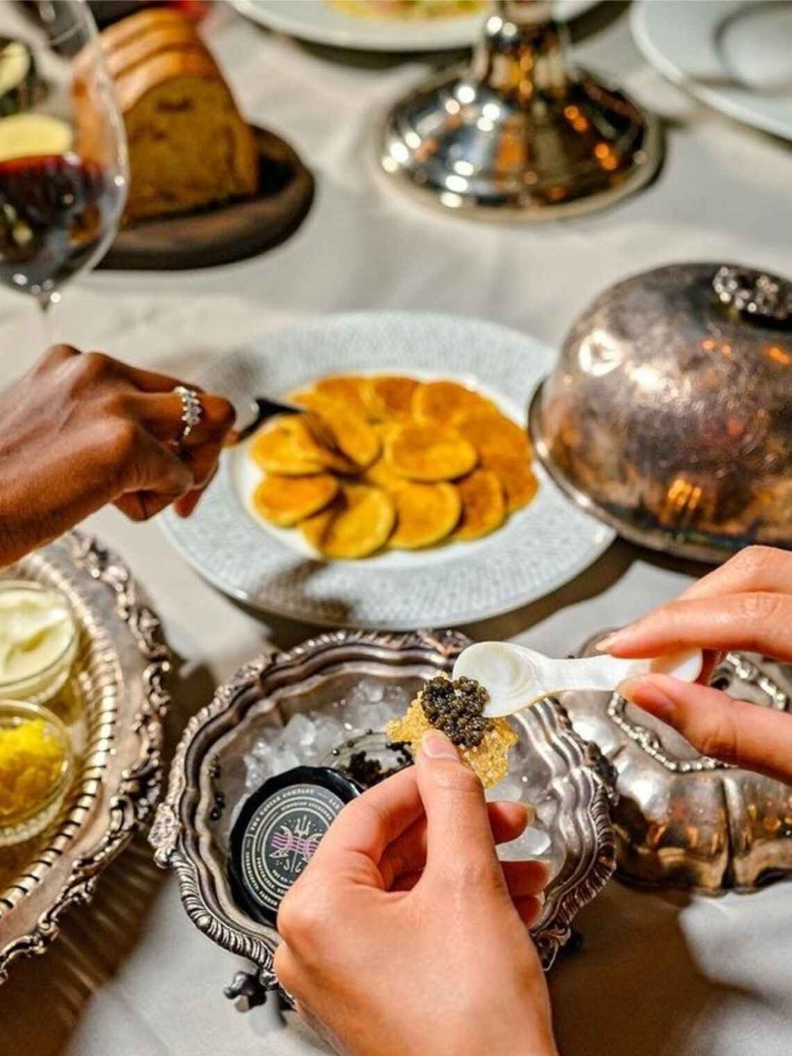 Person placing caviar on a crisp next to blinis at Maple & Ash.