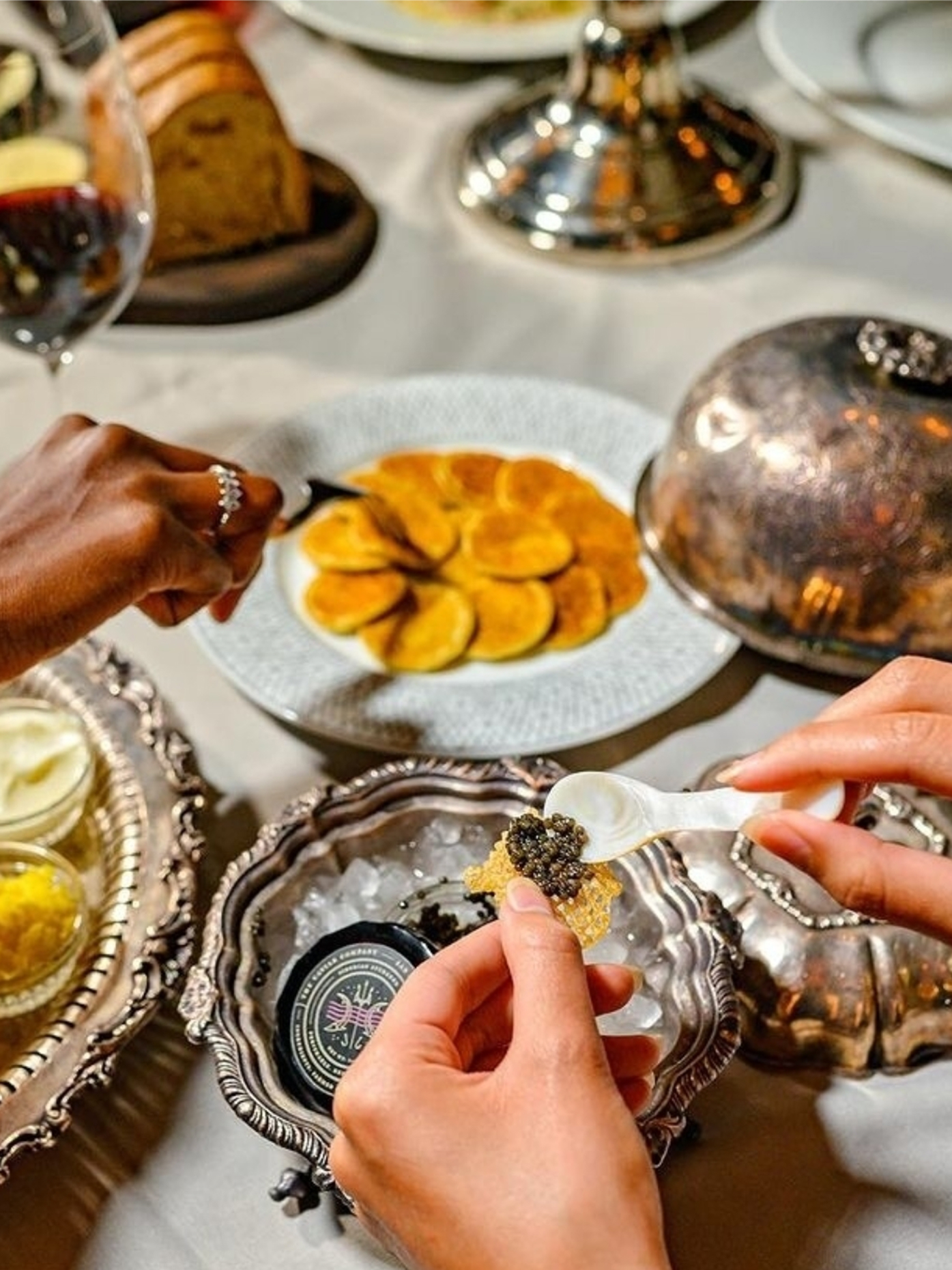 Person placing caviar on a crisp next to blinis at Maple & Ash.