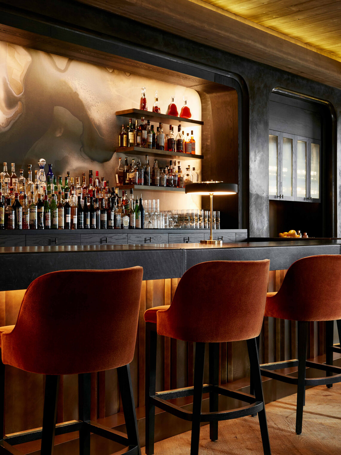 Maple & Ash steakhouse bar with velvet stools and backlit spirits wall