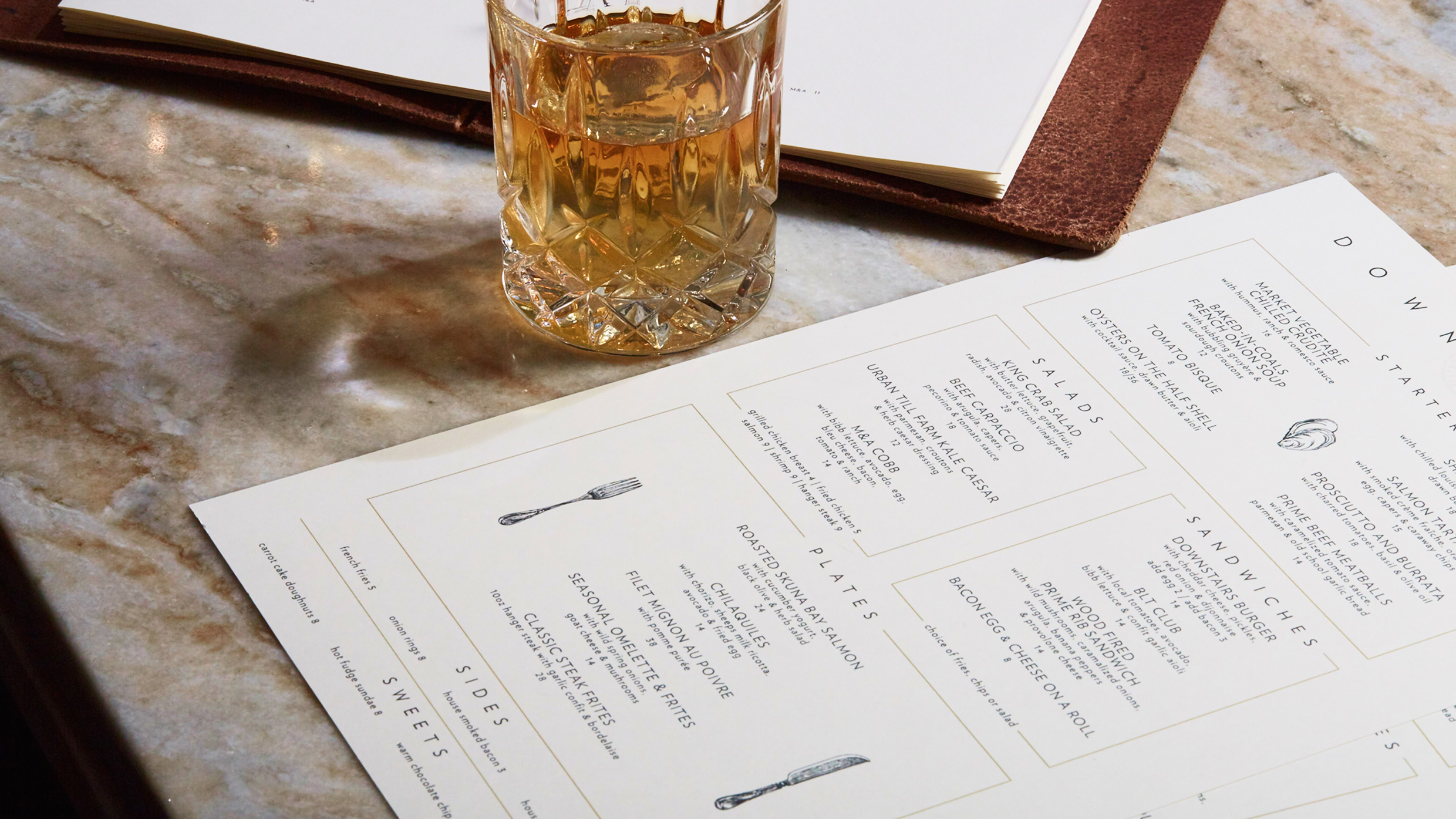 Maple & Ash downstairs menu with whiskey cocktail on marble surface