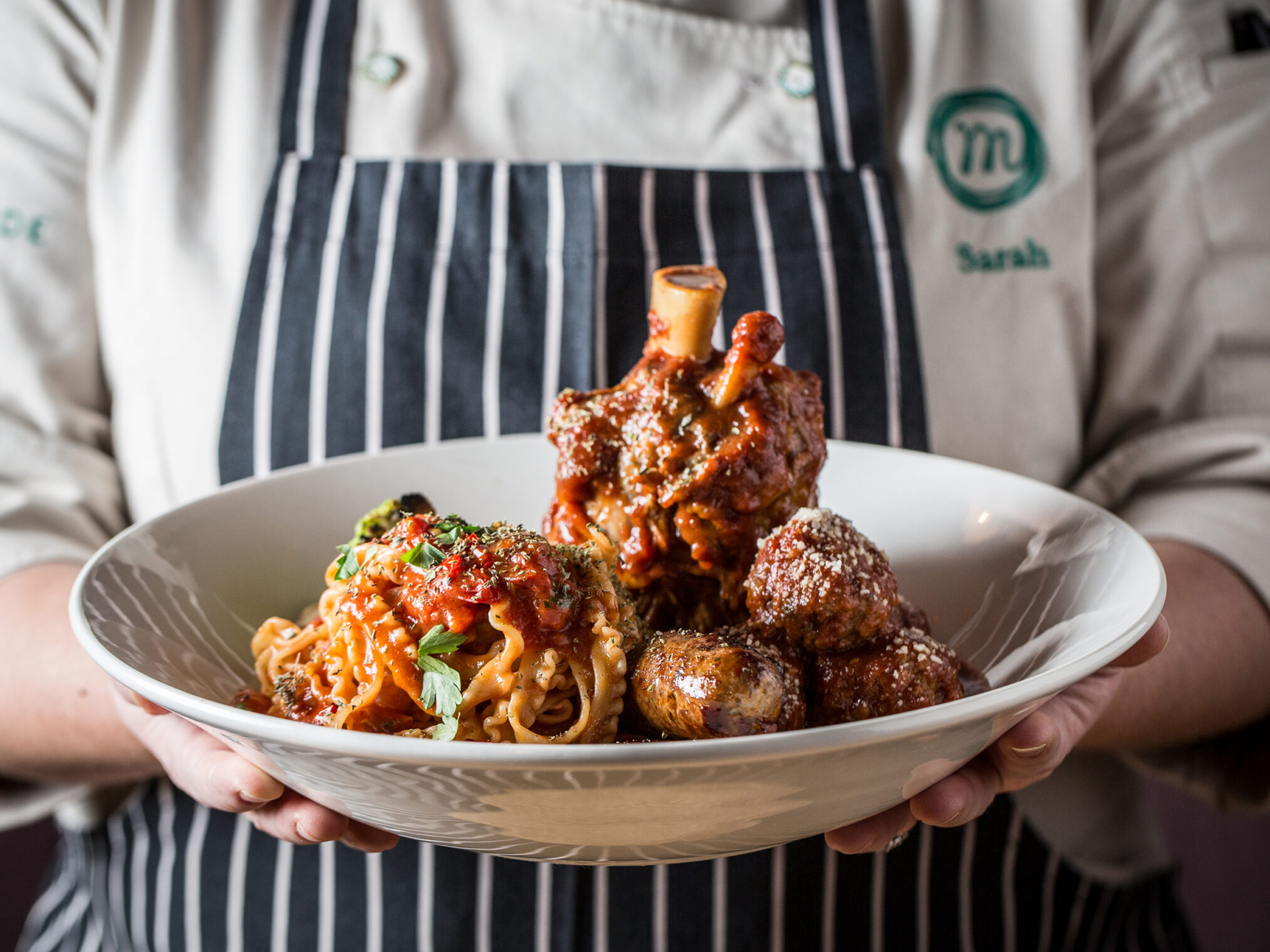 Chef holding a large bowl of Italian pasta, meatballs, and a braised shank.