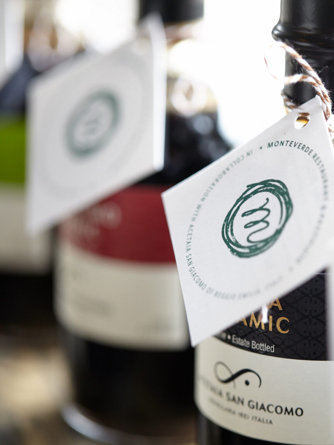 Close-up of Monteverde balsamic vinegar bottles with custom-branded white hanging tags.