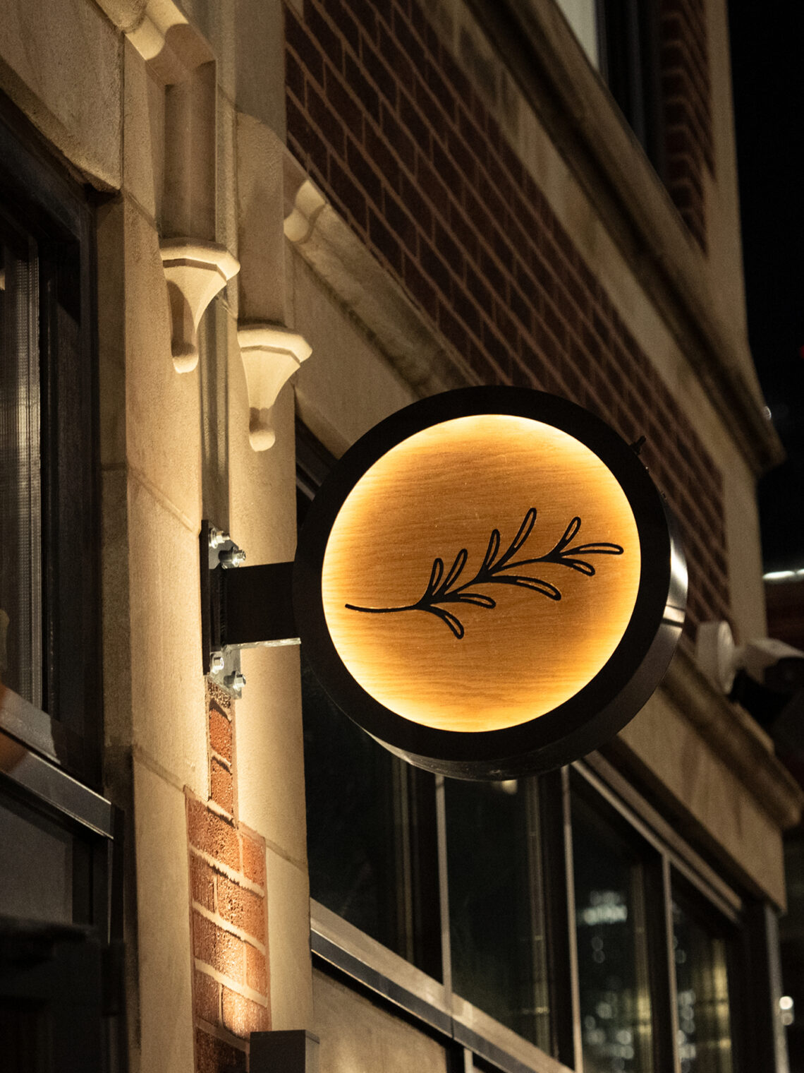 Illuminated circular exterior sign at night featuring Rose Mary's branch logomark.