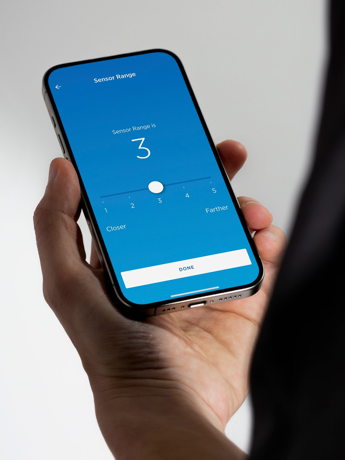 Close-up of a hand holding a smartphone showing the SloanConnect sensor range interface.