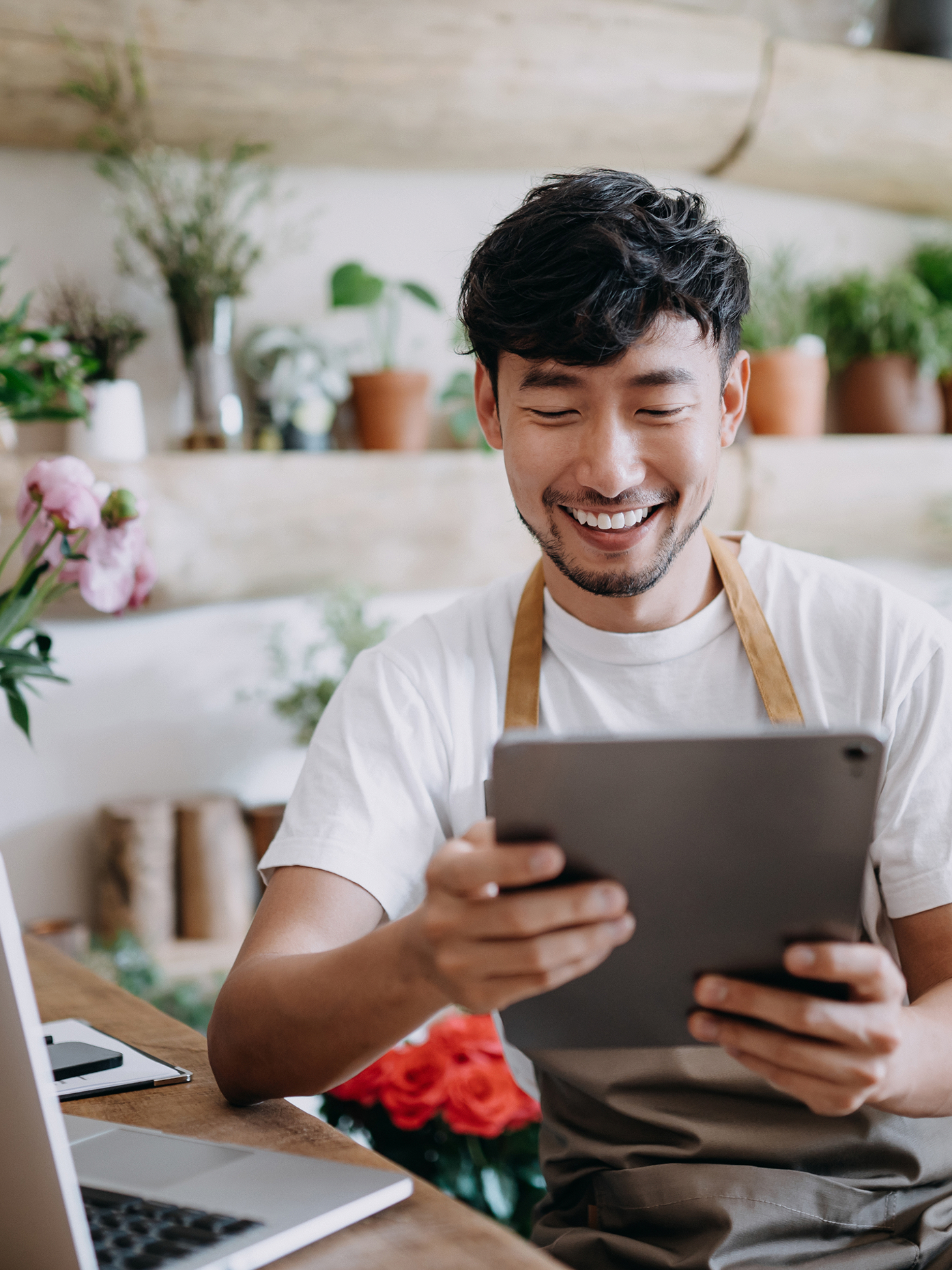 Smiling business owner wearing an apron and using a digital tablet.