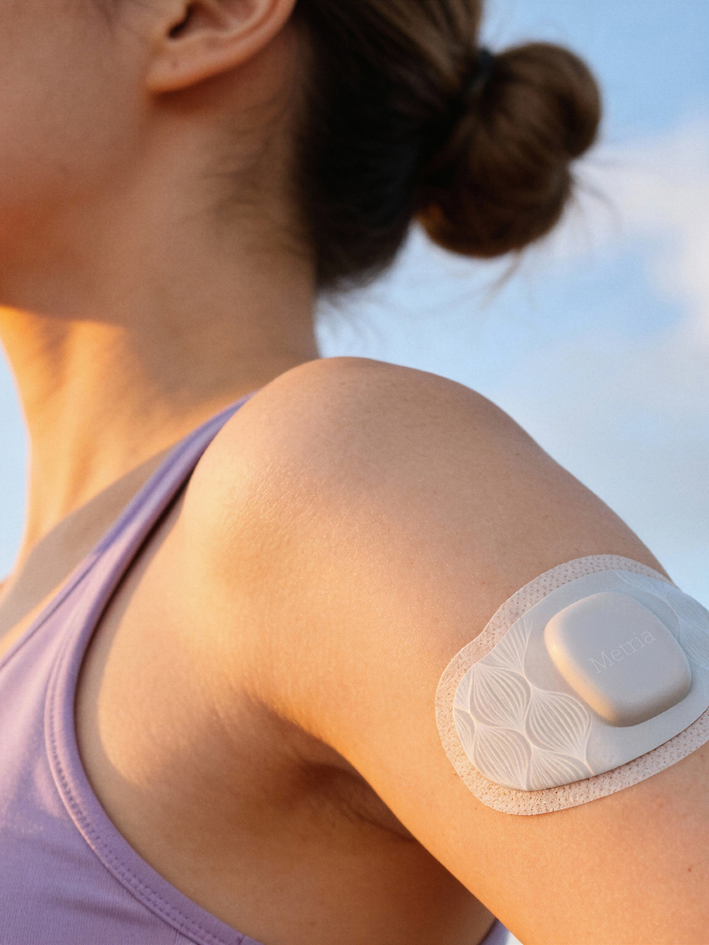 Close-up of a Metria continuous health monitor patch worn on a woman's arm.
