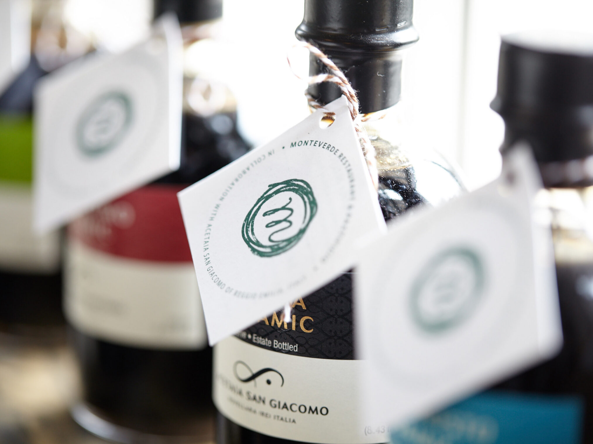Close-up of Monteverde balsamic vinegar bottles with custom-branded white hanging tags.
